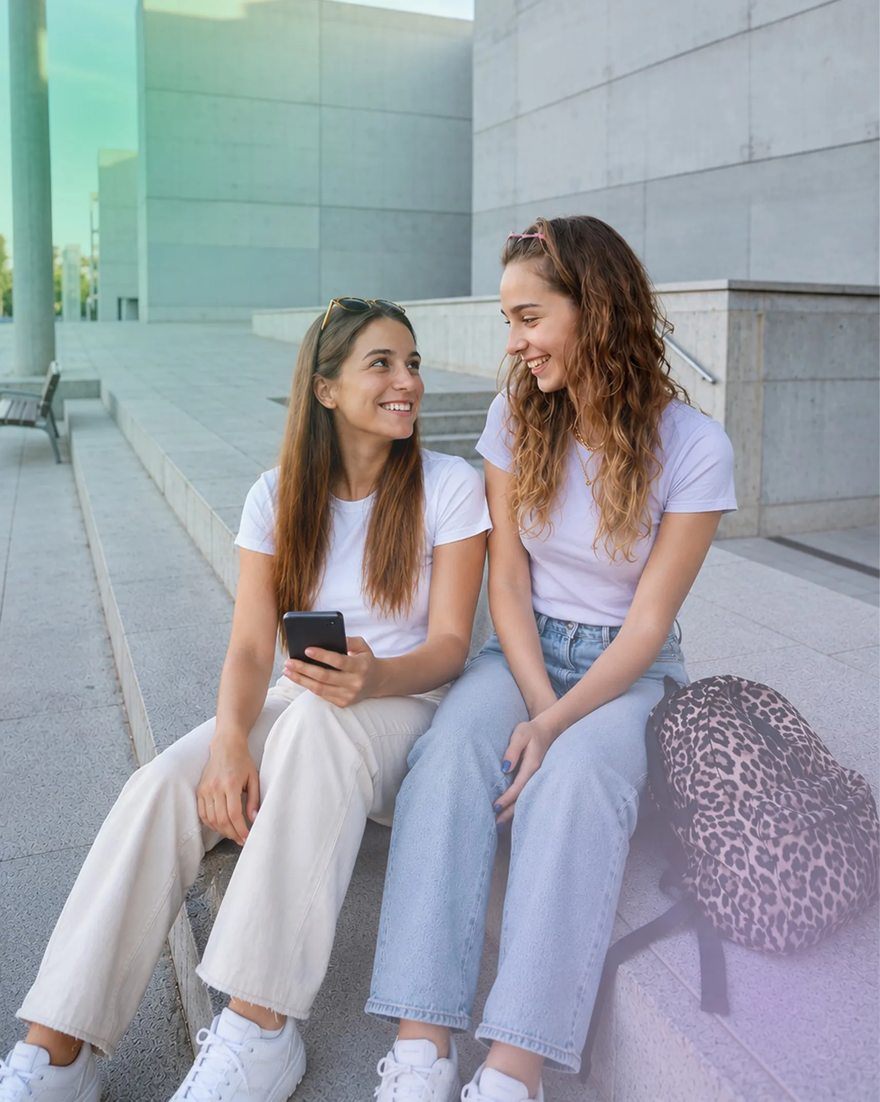 Dos jóvenes conversando en unas escaleras, una de ellas con el teléfono en la mano